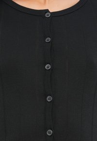 Κοντινό πλάνο μαύρου ριμπ ύφασματος με πέντε μικρά μαύρα κουμπιά δεμένα κατά μήκος του κέντρου μπροστά.