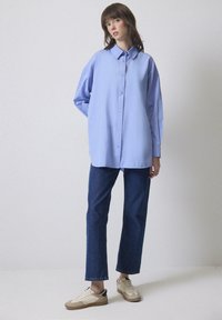 Cămașă bleu deschis, cu un croi lejer, având guler ascuțit și mâneci lungi. Asortată cu blugi negri și adidași.