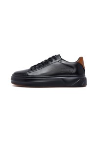 Sneaker in pelle nera con suola spessa, punta arrotondata, lacci neri e linguetta del tallone marrone, mostrato di profilo su sfondo bianco.