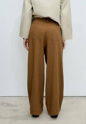 Wide-leg trousers in brown fabric with a smooth texture, featuring two back pockets and a high waist. Above, a slightly oversized beige top.