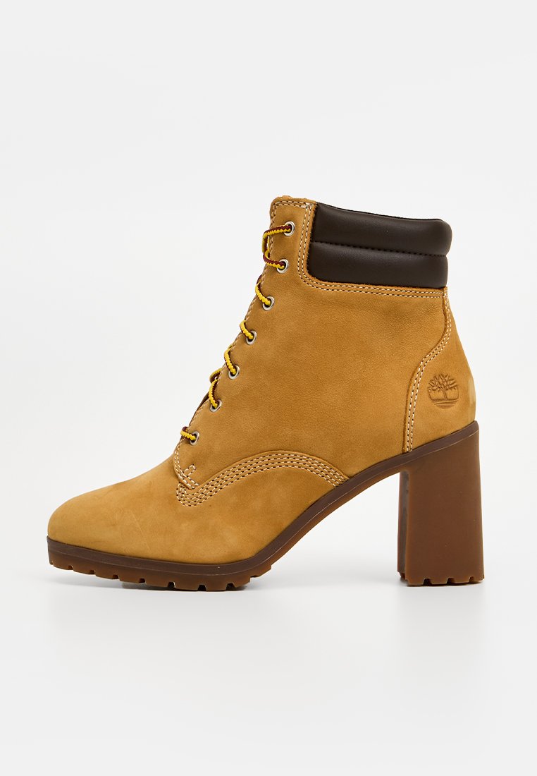 Stivaletti in suede marrone con tacco a blocco alto, punta rotonda, occhielli in metallo e colletto nero a contrasto. Logo distintivo sul lato.