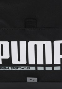 Juodas sportinis krepšys su baltu "PUMA" logotipu ir tekstu "ORIGINAL SPORTSWEAR". Rodyklė turi tekstūruotą audinį ir etiketę su pilku pumos logotipu.