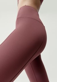 Vysoké legíny v hlbokej burgundskej farbe vyrobené z hladkej, elastickej tkaniny, s plochými švom a prúdnicovým dizajnom.