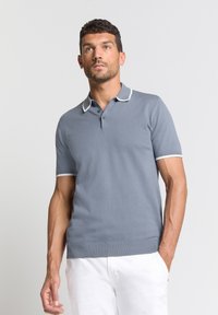 Grijze polo met korte mouwen, voorzien van een witte bies op de kraag en mouwen, met drie knopen bij de hals. Zachte textuur en een getailleerd ontwerp.