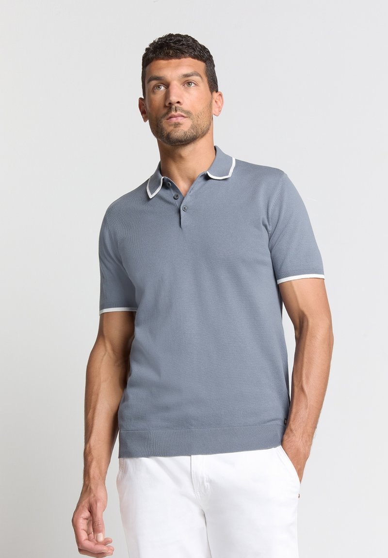 Grijze polo met korte mouwen, voorzien van een witte bies op de kraag en mouwen, met drie knopen bij de hals. Zachte textuur en een getailleerd ontwerp.