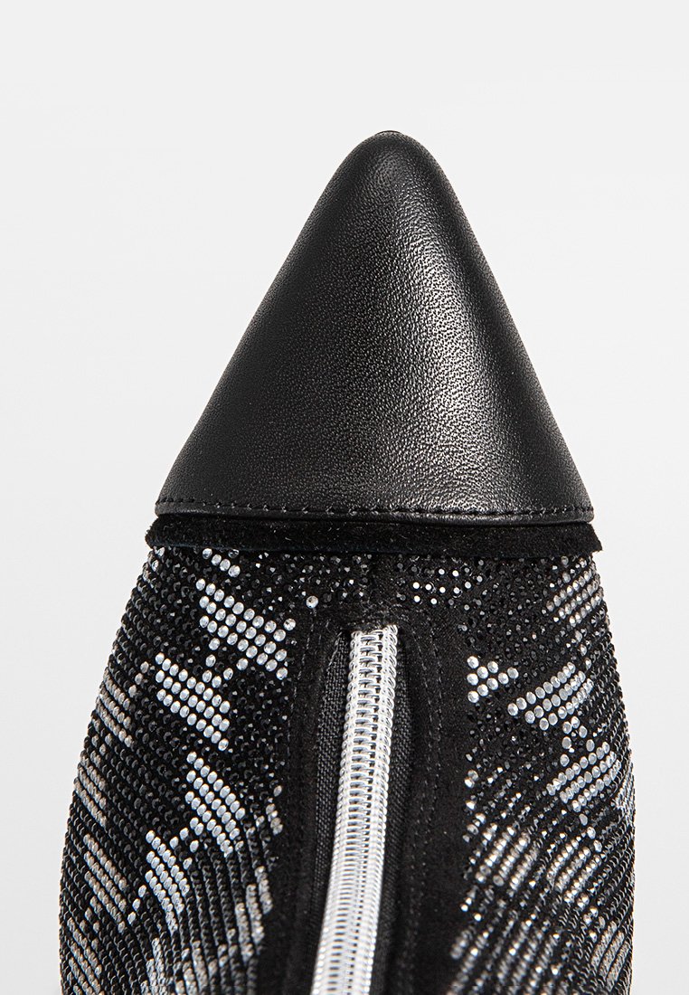 Zapato negro de punta afilada con parte superior texturizada adornada con strass plateados, un zipper interior y una puntera de cuero suave.
