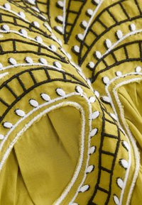 Tissu jaune présentant une broderie noire et blanche élaborée avec des motifs courbés et linéaires. La texture semble douce et détaillée.