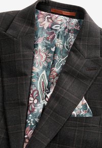 Veste blazer à carreaux gris avec un tissu lisse et texturé. Dotée d'une doublure florale colorée et d'un mouchoir de poche assorti.