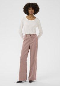 Prostrane, s visokim strukom, ružičaste hlače s gumbom sprijeda. Uparene s dugim bijelim topom s dugim rukavima. Glatka tekstura; crne cipele s oštrim potpeticama.