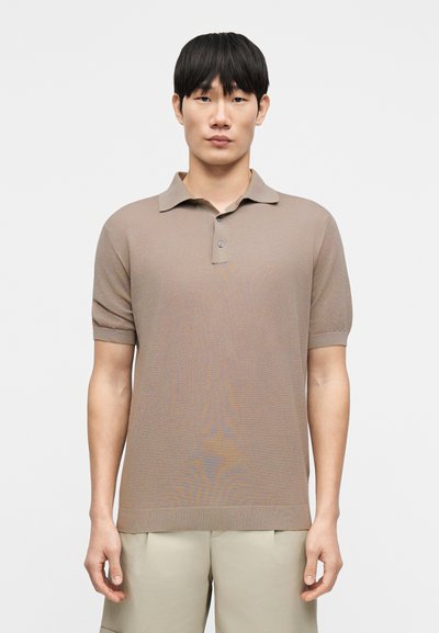 Polo beige à manches courtes avec col, présentant un design en maille texturée et une fermeture à un bouton au niveau du col.