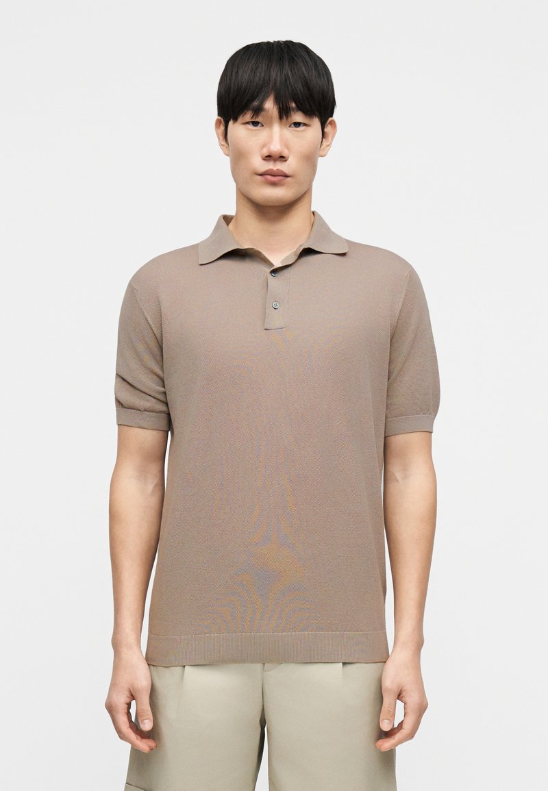 Μπεζ πόλο μπλουζάκι με κοντά μανίκια και γιακά, με υφασμένη πλεκτή υφή και ένα κουμπί στο λαιμό.