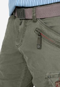 Olive green cotton cargo shorts with a textured finish, featuring a zippered pocket with red accent, and a woven brown belt with a logo buckle.