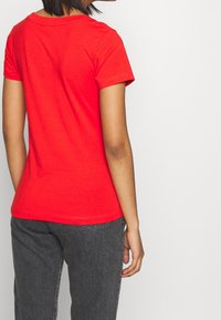Červené tričko s krátkým rukávem a kulatým výstřihem, vyrobené z měkké bavlny. Má přiléhavý střih a hladkou, rovnoměrnou texturu.