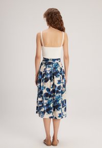 Top bianco con spalline sottili abbinato a una gonna lunga fino al ginocchio con un motivo floreale blu su uno sfondo crema, con dettagli plissettati.