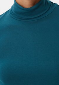 Tüllfarbener Rollkragenpullover aus weichem, dehnbarem Stoff mit glatter Textur und umgeschlagenem Kragen, der eine enganliegende Passform aufweist.