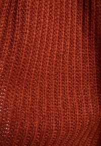 Pull en maille couleur orange rouille, présentant un côtelé vertical et une surface douce et texturée. Tissu légèrement étiré avec une apparence confortable.