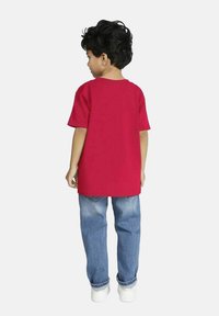 Rød bomulds T-shirt med korte ærmer, parret med blå denim jeans, set bagfra. Hvide sneakers fuldender outfittet.
