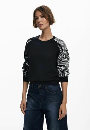 Felpa nera a maglia con motivo astratto bianco sulle maniche, dotata di scollatura rotonda e polsini a costine, abbinata a jeans blu.