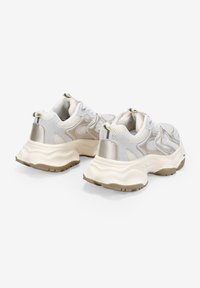 Zapatillas blancas y plateadas con parte superior de malla, diseño en capas, detalles texturizados y una suela gruesa color crema con un acento beige.