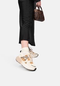 Zapatillas beige y marrón con acentos de estampado animal, tela texturada y suelas gruesas. Combinadas con una falda de satén negra y un bolso de estampado de leopardo.