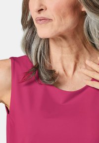 Fuchsia mouwloze top met een ronde halsline, gemaakt van soepele stof en met een ontspannen pasvorm. Model heeft grijs haar, licht gekruld.