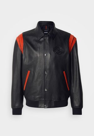 Chaqueta de cuero negro con acentos rojos en los hombros y bolsillos, puños y dobladillo acanalados, cierres de botón en el frente y detalle de logo grabado.