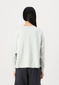 Světle šedá košile s dlouhým rukávem a kulatým výstřihem, volného střihu. Měkká látka se subtilní melírovanou texturou, zakončená žebrovanými manžetami.