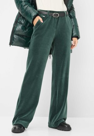 Groene corduroy wijde broek met zijzakken, gecombineerd met een zwarte riem en stevige zwarte schoenen; gedragen met een glanzende donkergroene pufferjack.