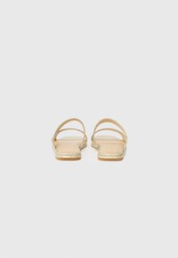 Gold flat sandals with two straps, a smooth interior, and a slight shimmer on the outsole. Minimalist design with open backs.