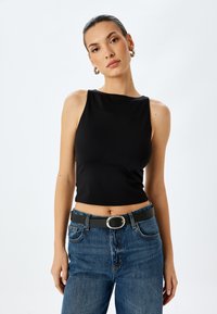 Zwarte mouwloze crop top van een gladde stof, gecombineerd met blauwe spijkerbroek met hoge taille en een zwarte riem met een zilveren gesp.