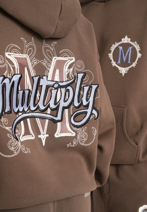 Brown sweatshirt featuring large embroidered "Multiply" text in blue and cream, with an ornate "M" on the back. Soft fabric and relaxed fit.