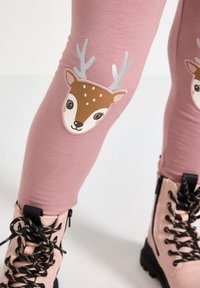 Pink leggings with a soft, stretchy texture feature a deer illustration on the knee. The deer has antlers and a friendly expression.