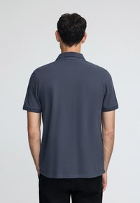 Granatowa koszulka polo z kołnierzykiem i krótkimi rękawami, wyróżniająca się fakturowanym materiałem i prostym wykończeniem, noszona z ciemnymi spodniami.