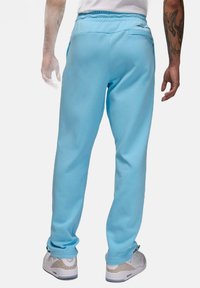 Jasnoniebieskie spodnie dresowe z elastycznym paskiem w talii, bocznymi kieszeniami i kieszenią z tyłu; gładka faktura. Noszone z jasnymi trampkami.