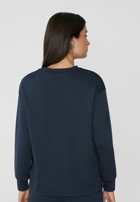 Granatowy sweatshirt z okrągłym dekoltem, długimi rękawami i gładką teksturą. Prosty design bez widocznych wzorów czy elementów metalowych.