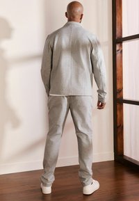 Felpa grigia chiara e pantaloni abbinati con una vestibilità comoda, realizzati in tessuto morbido, con dettagli sulle cuciture laterali e polsini a costine.