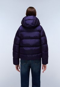 Kurtka puchowa w ciemnym fioletowym kolorze, z kapturem, pikowanymi sekcjami i krótkim krojem. Połączona z niebieskimi dżinsami.