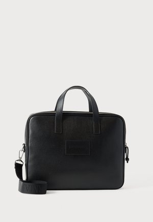 Czarna skórzana torba na laptopa z dwoma górnymi uchwytami, odpinanym paskiem na ramię, teksturowaną powierzchnią i prostokątnym kształtem. Widoczna wytłoczona łatka z logo.