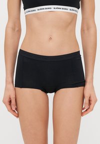 Fekete pamut alsónemű, bokszertípusú fazonban, logós derékpánttal, sima textúrával és testhezálló kialakítással. Nincsenek látható minták vagy kiegészítők.