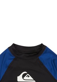 Čierny a modrý krátky rukáv rash guard s vysokým golierom; na prednej strane má biele logo vlna a ploché švy pre zvýšenú odolnosť.