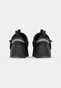 Chaussures de sport noires avec une tige texturée, des accents réfléchissants, des languettes au talon pour un enfilage facile, et une semelle en caoutchouc solide.