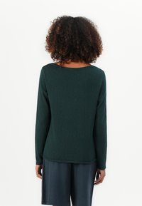 Dark green long-sleeve sweater with a relaxed fit, round neckline, and textured fabric, paired with dark shorts.