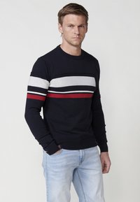 Pulover marin cu guler rotund, în dungi orizontale de gri, alb și roșu. Fabricat dintr-o tricotare texturată, cu manșete și tiv ribant.