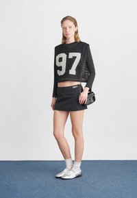 Czarny siateczkowy top do kroku z białą cyfrą "97", czarna mini spódnica, białe skarpetki i srebrne buty. Cechy szczególne: sportowy design i dopasowany fason.