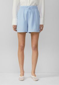 Shorts en coton bleu clair avec une taille élastique et un cordon de serrage. Présentent une finition texturée et des poches latérales. Associés à des chaussures slip-on en maille blanches.