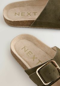 Olijfgroene suède instapsandalen met een kurken zool, voorzien van een metallic gouden gesp en een textuur voetbed. "NEXT" logo ingebrand aan de binnenkant.