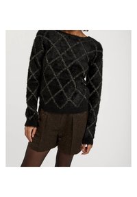 Czarny puszysty sweter z wzorem w diamenty, ozdobiony metalicznymi nitkami. W komplecie z teksturowanymi brązowymi szortami. Długie rękawy z prążkowanymi mankietami.