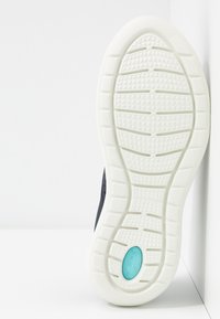 Chaussure noire avec une semelle blanche texturée. La semelle présente un accent circulaire bleu et des motifs géométriques pour l'adhérence.