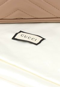 Article en cuir beige avec une couture visible au-dessus d'une doublure intérieure en tissu blanc présentant une étiquette bordée de noir avec le texte "GUCCI".