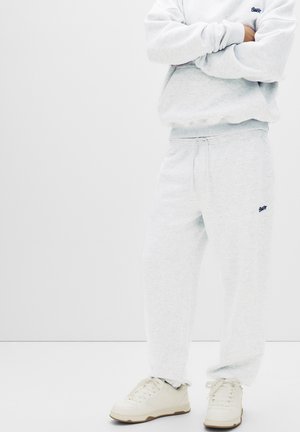 Light gray sweatshirt and matching sweatpants made of soft fabric, featuring a small logo on the chest and side, paired with white sneakers.